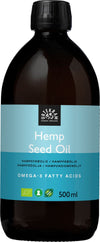 A dark, cylindrical bottle with a matte finish and a blue rectangular label. The label displays sans-serif white text: “Urtekram Organic Hemp Seed Oil, Omega-3 Fatty Acids, 500 ml.” Three small icons indicate organic, vegan, and nutrition certifications. The background is plain white. No people or actions are present in the image. A dark bottle with a blue label reading Urtekram Organic Hemp Seed Oil, Omega-3 Fatty Acids, 500 ml, featuring icons for organic, vegan, and nutrition certification. This
