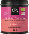 A 60g tin of Urtekram Tandoori Spice Mix, labeled organic. The container is cylindrical with a matte silver lid and has pink and orange paper packaging. The label features both bold and regular sans-serif fonts. Visible text includes uses for Indian food, casseroles, naan, and ingredients like garlic, cinnamon, cayenne. Item is set against a plain white background; no people or hands are present.