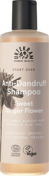 A bottle of Urtekram Anti-Dandruff Shampoo, Sweet Ginger Flower, featuring vegan and organic certifications, with ingredients like Panax ginseng root extract and aloe vera, plus a beige cap. The bottle is cylindrical with a matte finish. Label uses modern sans-serif typography in white against an orange-brown background. No people or hands present. Set against a plain white backdrop in a centered product shot.