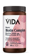 A brown plastic bottle labeled VIDA Beauty Biotin Complex with 5000 µg of biotin, calcium, zinc, and vitamin C. This supplement supports thick hair and strong nails. The bottle contains 100 capsules, and the label is mostly white and pink. Matte finish on bottle surface; cylindrical shape with a screw cap; sans-serif font dominates the label; shot shows only the product against a plain white background with no people or additional objects visible.