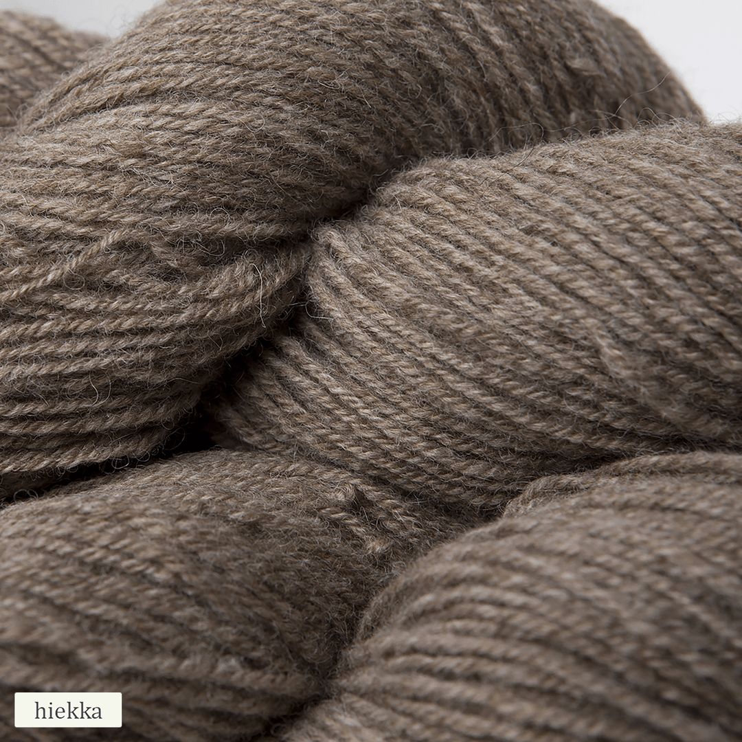 Close-up of several skeins of light brown, textured alpaca yarn with visible fibers. The yarn has a matte finish and is loosely wound into round skeins. A small label in the corner reads “hiekka,” which means sand in Finnish, indicating the color or shade of the yarn. Background appears neutral and plain. No people or hands visible in the image.