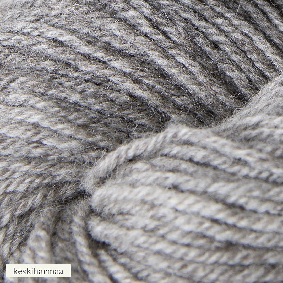 A close-up view of light gray yarn, showing its soft texture and twisted fibers. The yarn is matte and fibrous with a loose twist visible in the strands. In the lower left corner, there is a small label with the text keskiharmaa in simple, clear typography. There is no visible packaging apart from the label. No people or hands are present in the image.