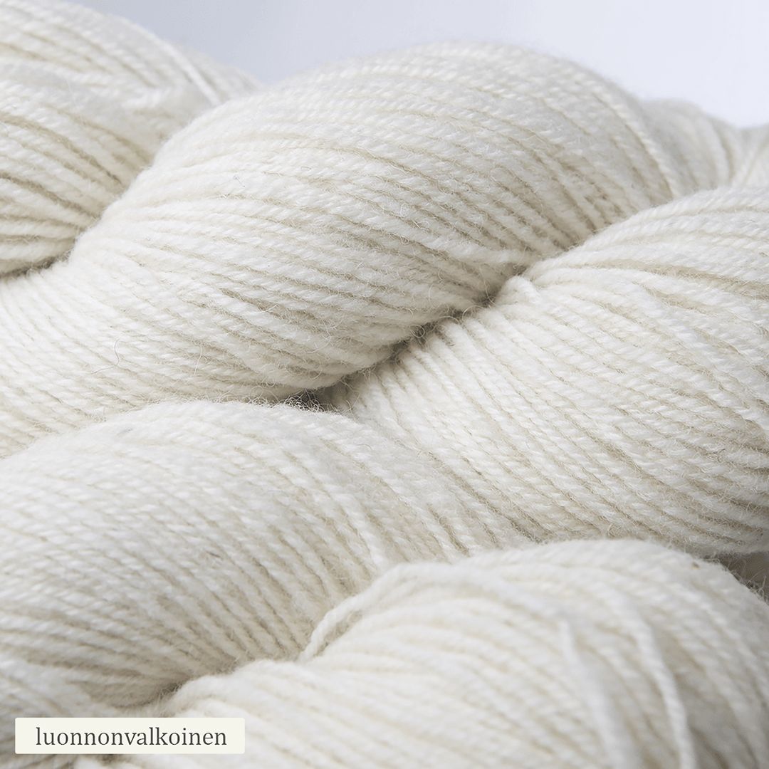 Close-up of three skeins of natural white yarn, twisted and soft in texture. The yarn is unbleached with a matte surface. A small paper label appears in the corner with the text “luonnonvalkoinen” in plain font. No packaging beyond the label is visible. The background is neutral and uncluttered, no people or hands are present.