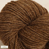 A close-up of a skein of brown yarn, coiled neatly with visible texture. The yarn has a matte finish and is cylindrical in shape. A small rectangular label with the word “suklaa” is placed at the bottom left corner in simple sans-serif lettering. No people or hands are present, and the background is plain.
