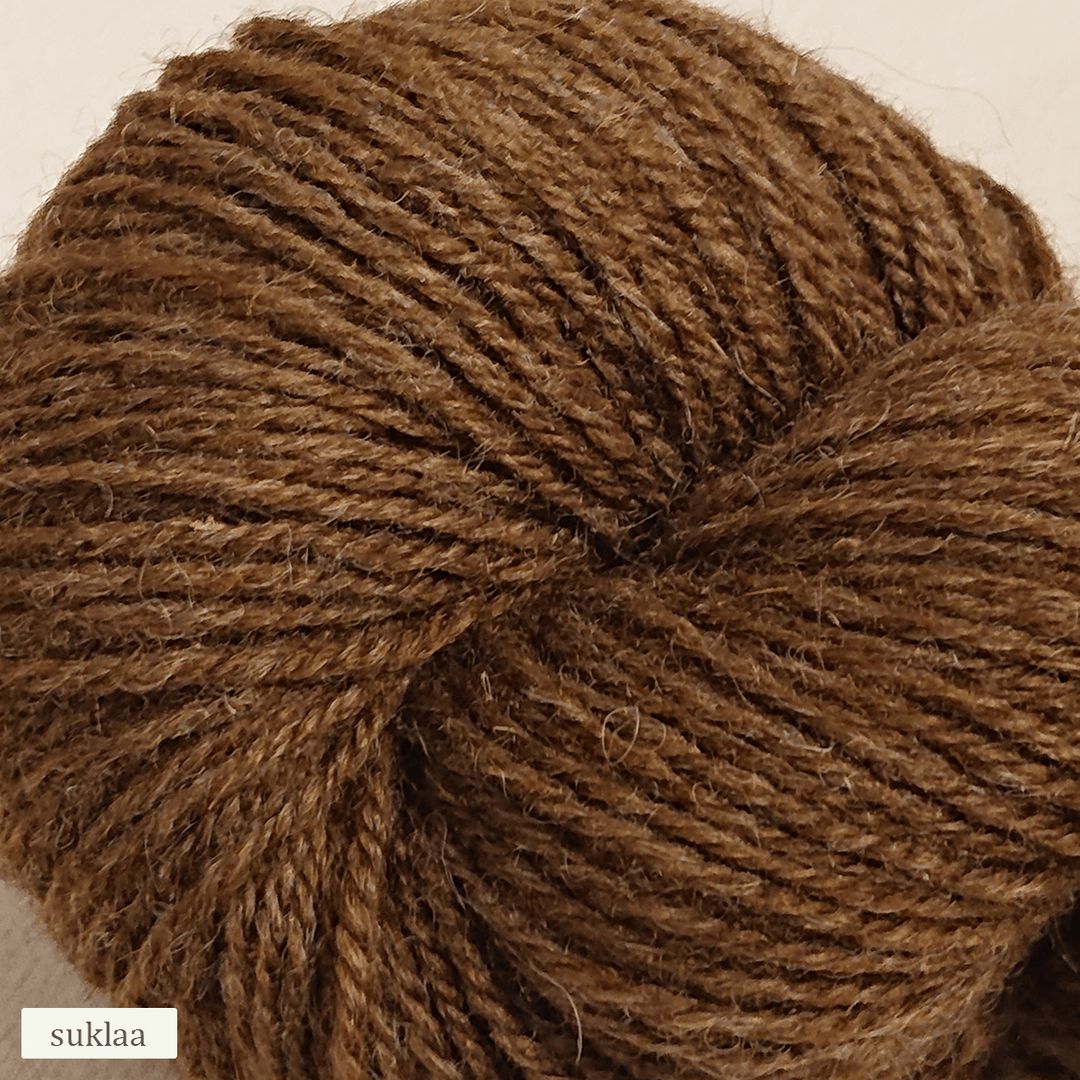 A close-up of a skein of brown yarn, coiled neatly with visible texture. The yarn has a matte finish and is cylindrical in shape. A small rectangular label with the word “suklaa” is placed at the bottom left corner in simple sans-serif lettering. No people or hands are present, and the background is plain.