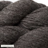 Close-up of thick, dark gray yarn skeins with a soft, slightly fuzzy texture. Multiple rounded skeins are tightly wound with visible fibers. Surface is matte. Yarn appears unwrapped and not in commercial packaging. A small, unobtrusive label in the corner has simple sans-serif text reading tummanharmaa. Plain background. No people or hands present.