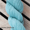 A skein of light blue-green yarn rests on wooden slats. The yarn is wound in a classic hank shape, with a matte finish and no visible packaging. The text “Vaalea sinivihreä” appears in the bottom left corner in clear, white sans-serif font. No people, hands, or actions are visible. Shot is taken from above against a wooden background.