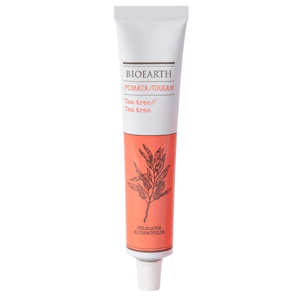A tube of Bioearth Pomata/Cream labeled Tea tree, featuring a botanical illustration and a white cap on the bottom, highlights the natural benefits of tea tree oil. The tube is cylindrical with a matte finish and mostly white exterior. Label includes “Bioearth” and “Tea tree” in clear sans-serif type. Botanical image shows green leaves. No people or hands are visible; plain light background; close-up product shot.