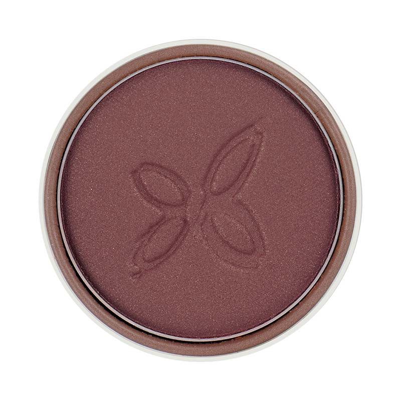 A round pan of mauve-colored powder blush features a subtle butterfly imprint in the center. Surface is matte with no visible shimmer. The product is inside a circular, metallic-looking compact without legible label text in frame. No hands or people are present. The background is plain and neutral, shot from above at close range.