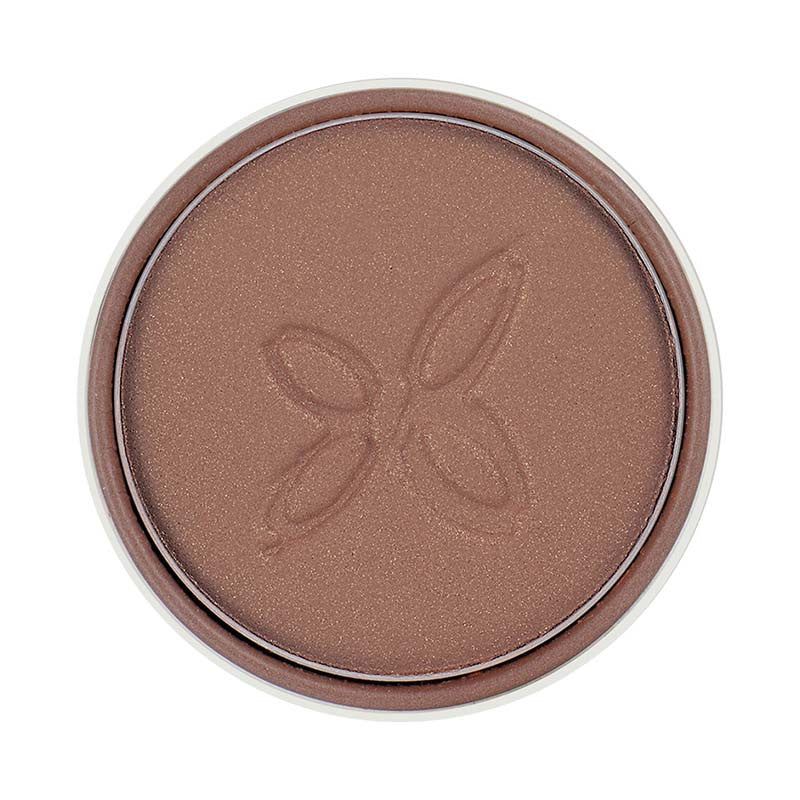 A round pan of brown pressed powder makeup with a subtle shimmer and a simple floral motif embossed in the center. The powder is contained in a circular metal pan, no lid or compact visible. There is no visible label text, typography, or brand marks. The surface shows a light-reflective finish. The background appears neutral and uncluttered with no people or hands present in the frame.