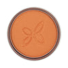 A round compact of shimmery orange powder makeup featuring a subtle embossed butterfly design in the center. The powder surface is smooth with a metallic sheen. Packaging is circular and plastic, color not specified. No visible typography or label text on product or packaging. Product placed against a plain, neutral background; no people or hands present in the image. Studio shot, close-up view.