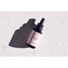 A small dark glass dropper bottle labeled Arctic Beauty Oil rests on a white surface, casting a soft shadow. The bottle is cylindrical with a black screw cap and attached dropper. The label has minimal text in clear, sans-serif lettering. The white background is untextured. This is a product-only shot with no people or props visible.