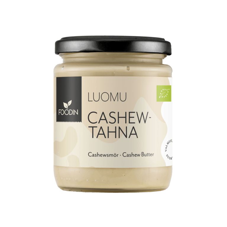 Foodin Luomu Cashewtahna -purkki, lasinen, musta kansi, beige etiketti, teksti suomeksi ja englanniksi; lihavoitu versaaliteksti brändinimelle, vaaleanbeigeä cashewtahnaa näkyvissä