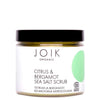 JOIK Organic Citrus & Bergamot Sea Salt Vartalokuorinta; kirkas purkki mustalla kierrekannella ja valkoisella etiketillä, vihrein elementein; kuvituksena sitrusta ja bergamottia, teksti englanniksi ja vironkielisenä; purkki sylinterinmuotoinen, sisällä karkeaa suolakuorintaa; groteskikirjasin etiketissä; neutraali studiotausta, ei ihmisiä tai käsiä.