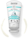 A tube of Lavera Basis Sensitiv Cleansing Gel with a splash of water, aloe, and jojoba illustrations is shown alongside product smears. The tube is white with blue-green accents and a glossy surface. Sans-serif black text on the label includes the product name and descriptors. The scene is well-lit with a plain background, flat lay composition, no people or hands present. Suitable for normal and combination skin, this vegan formula is also carbon neutral.