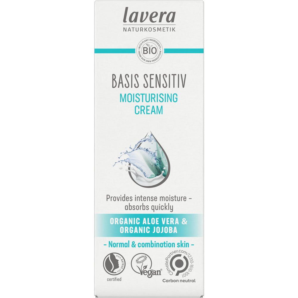 Front of a Lavera Basis Sensitiv Moisturising Cream box, highlighting organic aloe vera and jojoba for normal and combination skin. Features vegan, certified, and carbon neutral logos, emphasizing natural skincare. Rectangular cardboard box with a matte white finish and blue-green accents; product name in bold sans-serif type; icon-style certification logos on the lower section; plain studio background. No people or hands visible.
