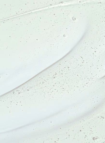Close-up of a translucent serum with small air bubbles suspended throughout, spread smoothly on a white surface. The serum has a glossy finish and is colorless. No packaging or label text is visible. Background is plain white with no additional objects, people, hands, or actions present in the image.