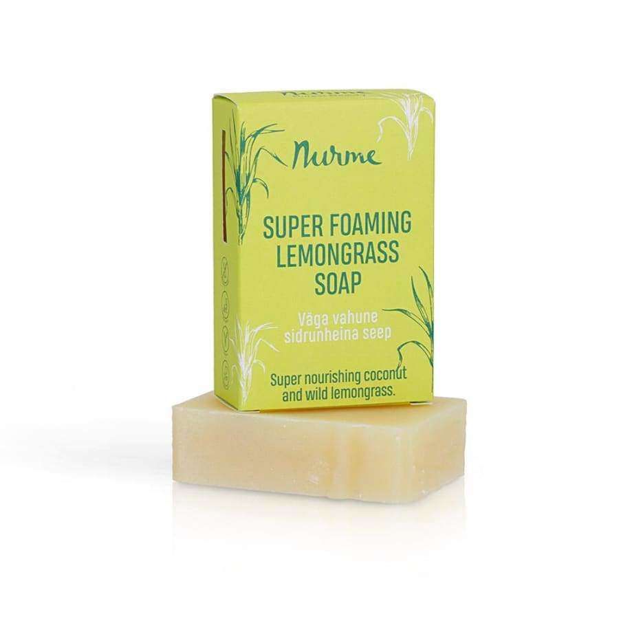 Nurme Sitruunaruoho -palasaippua, "Super Foaming Lemongrass Soap"; keltavihreä pystyssä oleva rasia beigen suorakulmaisen saippuapalan päällä; pakkaus mattapintainen, painettuja sitruunaruohokuvituksia; teksti mainitsee kookoksen ja villin sitruunaruohon; lihavoitua groteskitekstiä tuotenimelle; vaalea tausta, ei ihmisiä tai toimintaa; kuvattu edestäpäin.