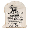 Olivos Vuohenmaitosaippua; kangaspussi tekstillä "Goat Milk Olive Oil Soap" ja vuohen kuvitus; teksti korostaa käsintehtyä Olivos-tuotetta englanniksi ja ranskaksi, mainiten vuohenmaidon ja oliiviöljyn ravitsevan yhdistelmän; pussi luonnonvalkoinen mustalla painetuin tekstein serifi- ja groteskikirjasimin; valkoinen tausta, ylhäältä kuvattu, ei ihmisiä tai käsiä.