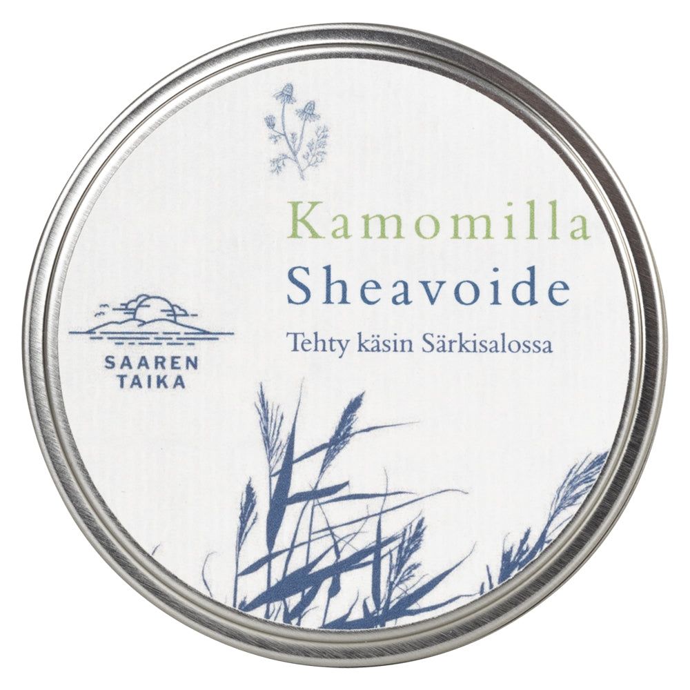 Saaren Taika Sheavoide Kamomilla; pyöreä hopeanvärinen metallipurkki mattapintaisena, kannessa teksti "Kamomilla Sheavoide" ja "Tehty käsin Särkisalossa"; paperietiketissä sinisiä kasvikuvia viivapiirroksena ja Saaren Taika -logo; kuvattu ylhäältä keskitetysti valkoisella taustalla, ei ihmisiä tai käsiä.