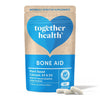 Together Health Bone Aid; sininen-beige mattapintainen pussi tekstillä "together health BONE AID" groteskityylillä, mainitaan kasvipohjainen kalsium, K2, D3 ja 72 mineraalia; kolme valkoista kapselia pussin edessä; neutraali tausta.