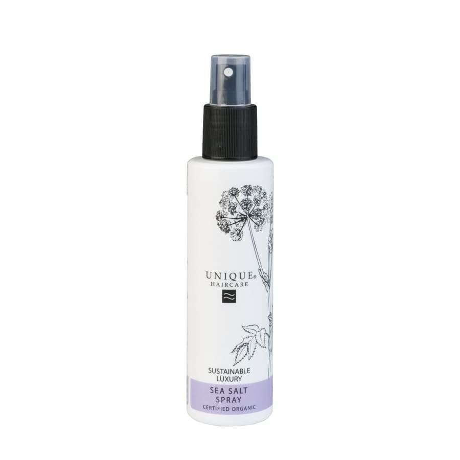 Unique Suolasuihke; valkoinen suihkepullo tekstillä "Unique Haircare Sea Salt Spray", musta korkki ja kasvikuvitus; pullo lieriömäinen mattapinnalla; etiketissä groteskitekstiä lihavoituna ja ohuena mustana kirjasimena, luettavissa "Sustainable Luxury" ja "Certified Organic" -ainesosat; tuote eristetty vaalealle, kevyelle taustalle studiokuvassa; ei ihmisiä.